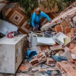 Uma pessoa está no meio de escombros de uma casa destruída pelas chuvas